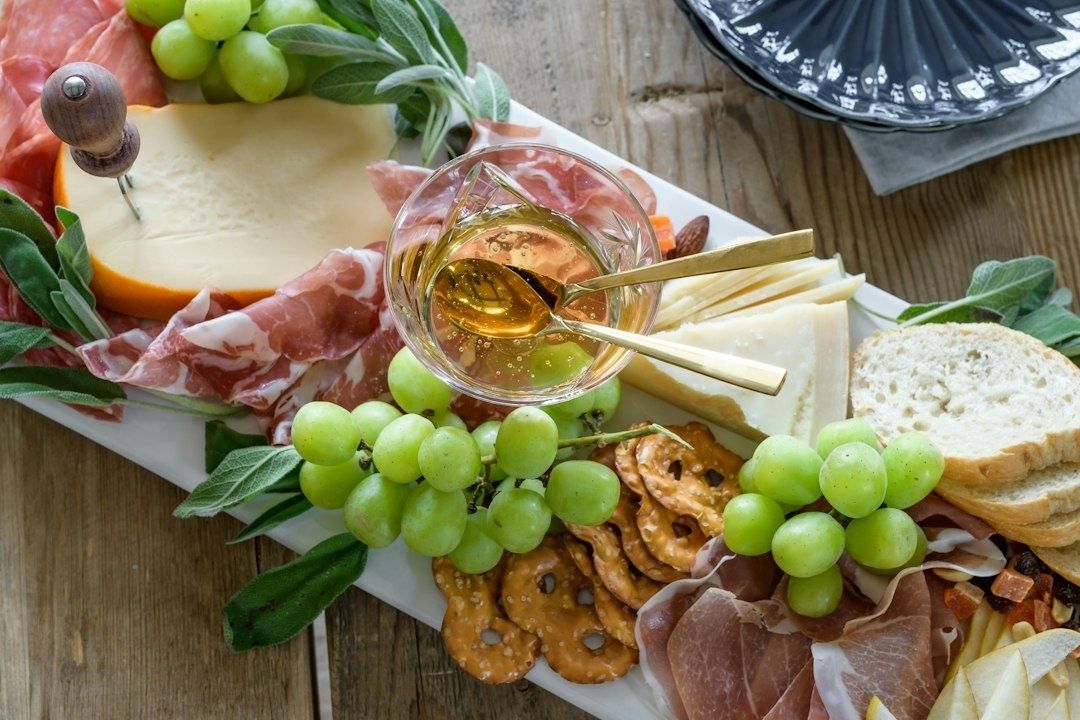 Ost- och charkbricka med vindruvor, bröd och ett glas gyllene dryck